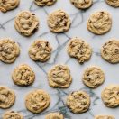 A top-down view of multiple chocolate chip cookies arranged evenly on a marble surface.