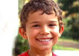 Brown-haired boy with big ears, white teeth, and short wavy hair